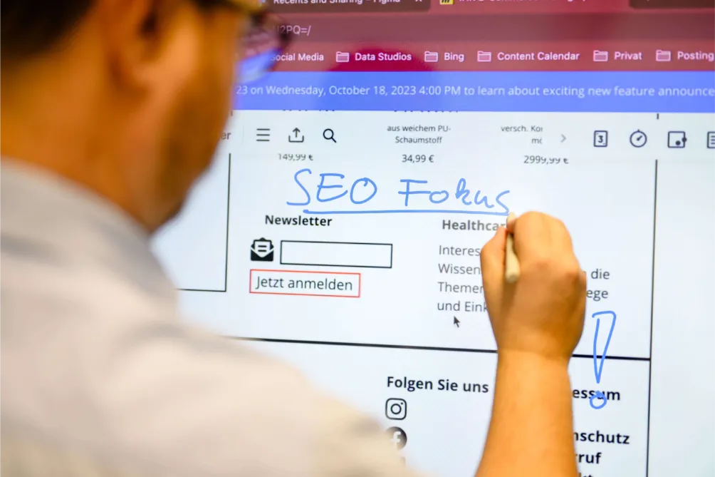 Person schreibt „SEO Fokus“ mit blauem Marker auf einem digitalen Whiteboard mit einer Webdesign-Köln-Website und Menüs.